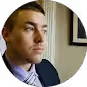 Side profile of a man with short hair wearing a suit and tie inside a room.